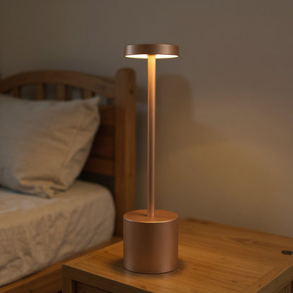 Lampe de chevet design cuivre allumée sur table de nuit en bois